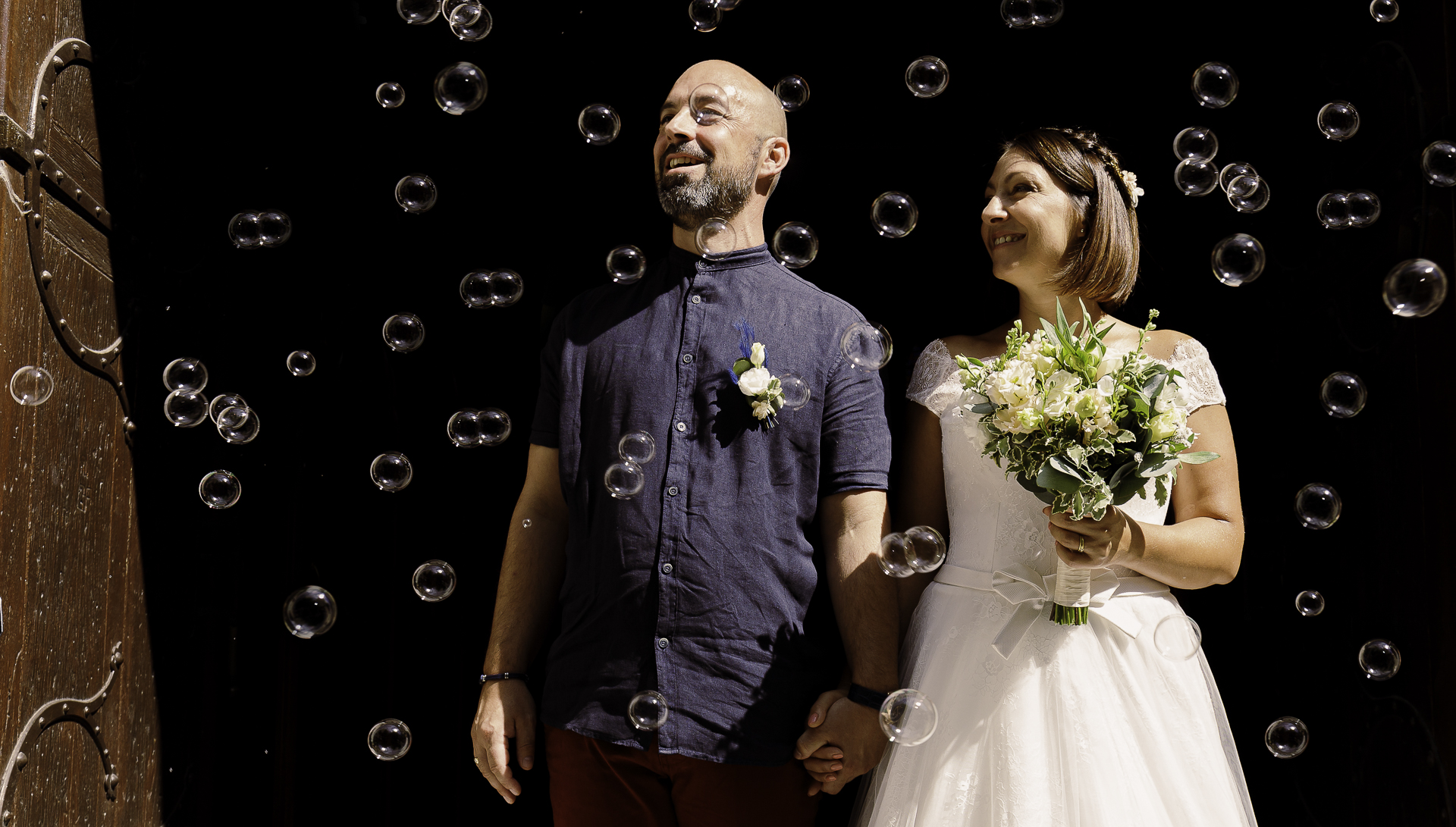 Photo d&apos;un couple de marié se tenant la main à la sortie de l&apos;église, entouré de bulles.