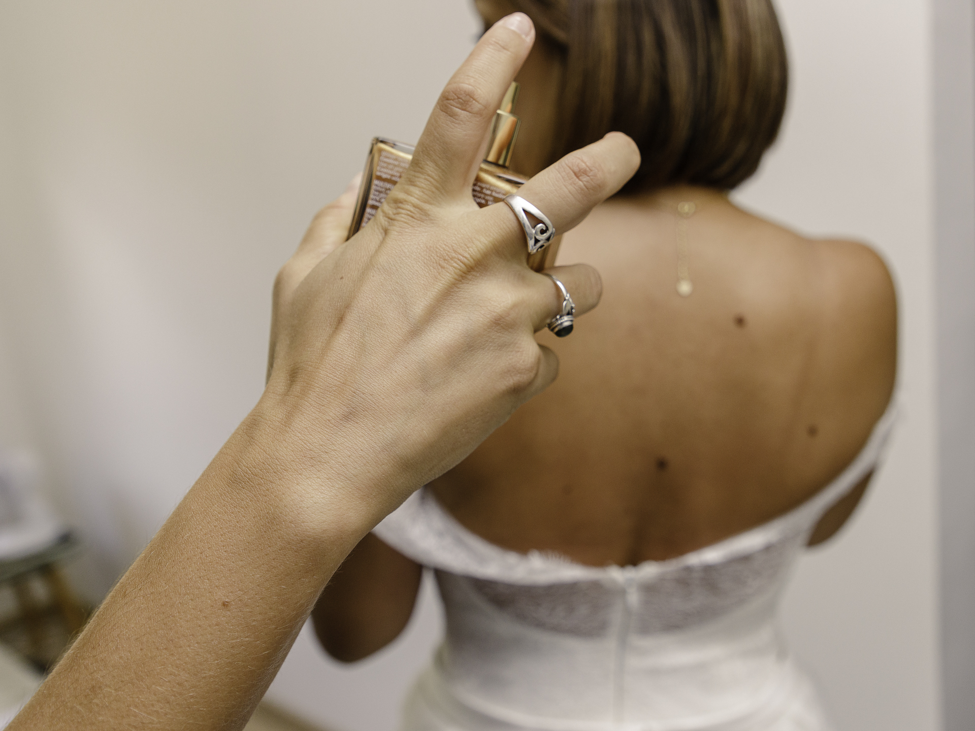 Une main vient en aide à la mariée pour compléter sa tenue. Elle tient une bouteille de parfum et s&apos;apprête à en appliquer à la mariée.