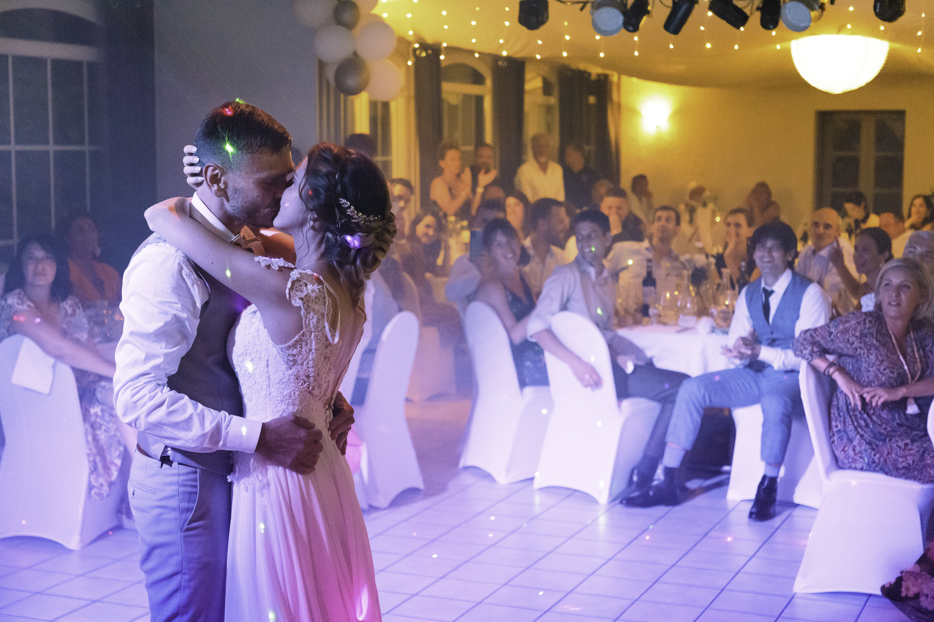photo des mariés prise lors de la soirée, à l&apos;ouverture du bal. Le couple s&apos;embrasse sur la piste, à la fin de leur première danse, devant leurs invités.