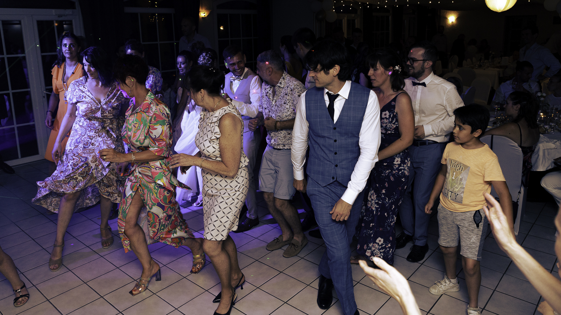 Photo d&apos;ambiance de la soirée de mariage. Les invités dansent ensemble dans les lumières du DJ.