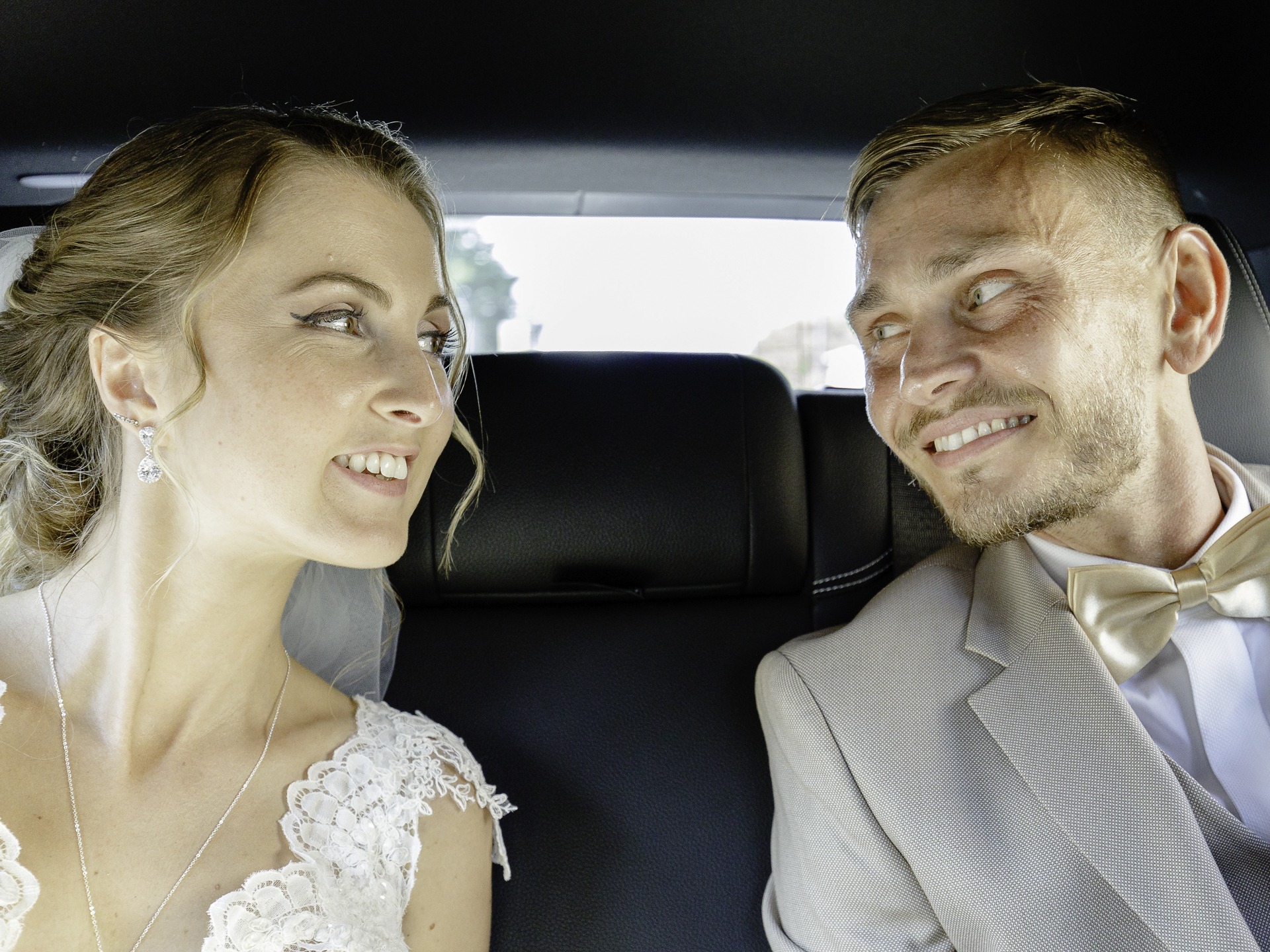 Un couple de marié se regarde amoureusement dans une voiture.